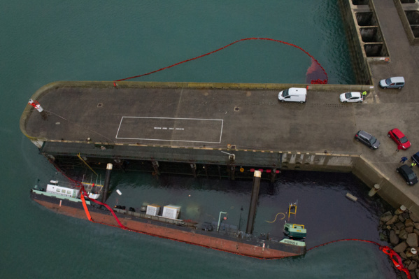 Comme on peut le voir sur cette photo aérienne prise ce lundi matin à bord de l'hélicoptère EC225, un barrage flottant de 300 mètres a été mis en place autour de la barge couchée et du ponton (Photo B.Planchais/Marine nationale)