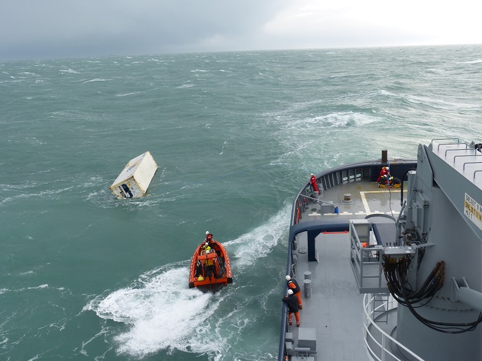 Un conteneur flottant en mer pris en charge par un remorqueur de la Marine